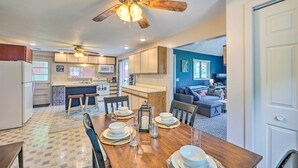 A modern kitchen with wooden cabinets, a dining table set with plates and glasses, and a ceiling fan. - Cottage on Tubbs Lake w/ Fire Pit Near Skiing! (Mecosta)