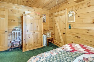 Una habitación de madera con una cama, un armario de madera, una silla y una pequeña mesa con una estantería.