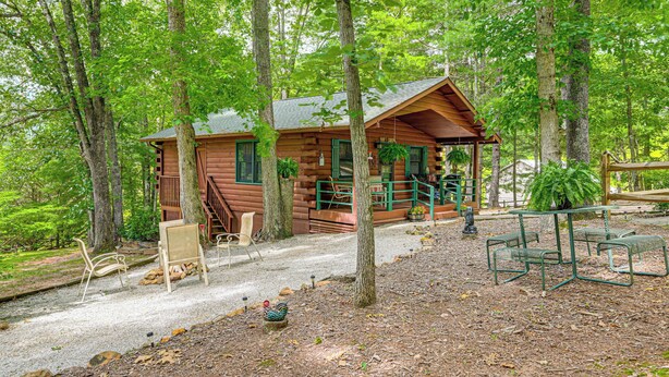 Ein rustikales Blockhaus mit Veranda, umgeben von Bäumen und Kieswegen.