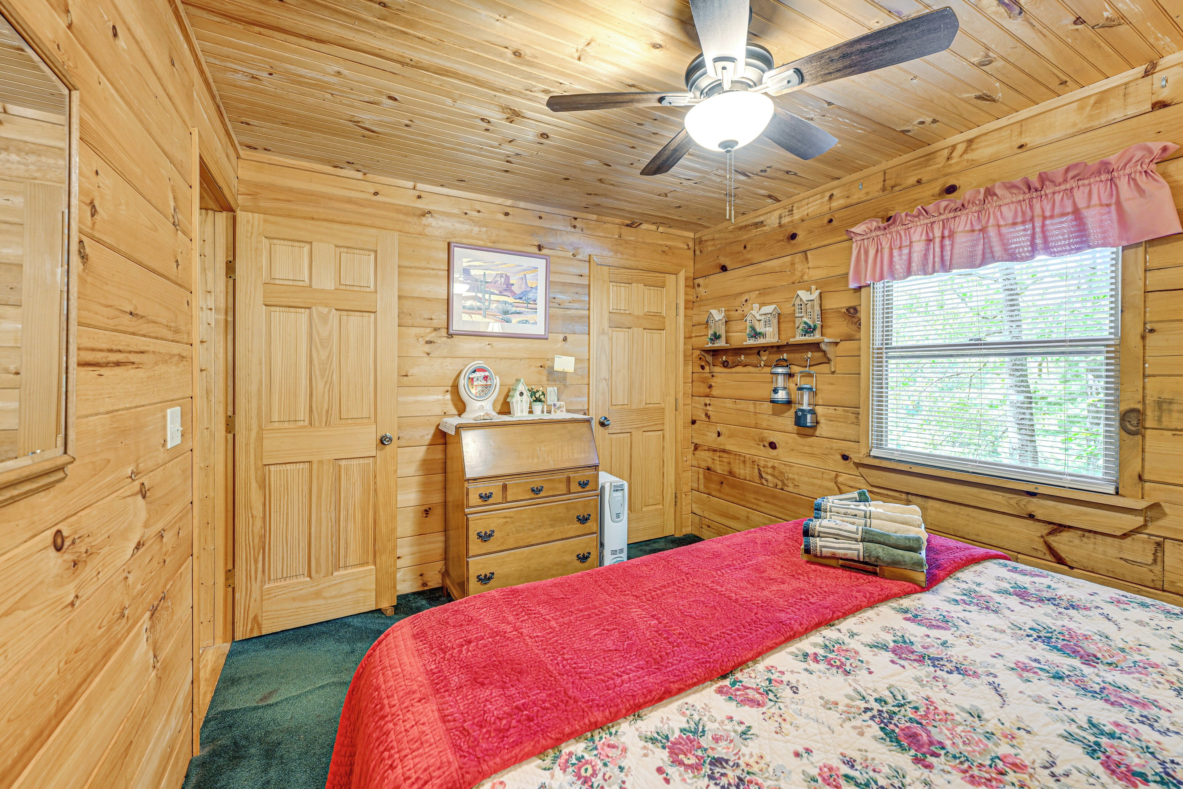 Un dormitorio de cabaña de madera con cama, cómoda y ventana con persianas.