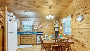 A wooden cabin interior with a kitchen, dining area, and a clock on the wall. - 11 Mi to Dtwn: Franklin Cabin w/ Porch! (Franklin)