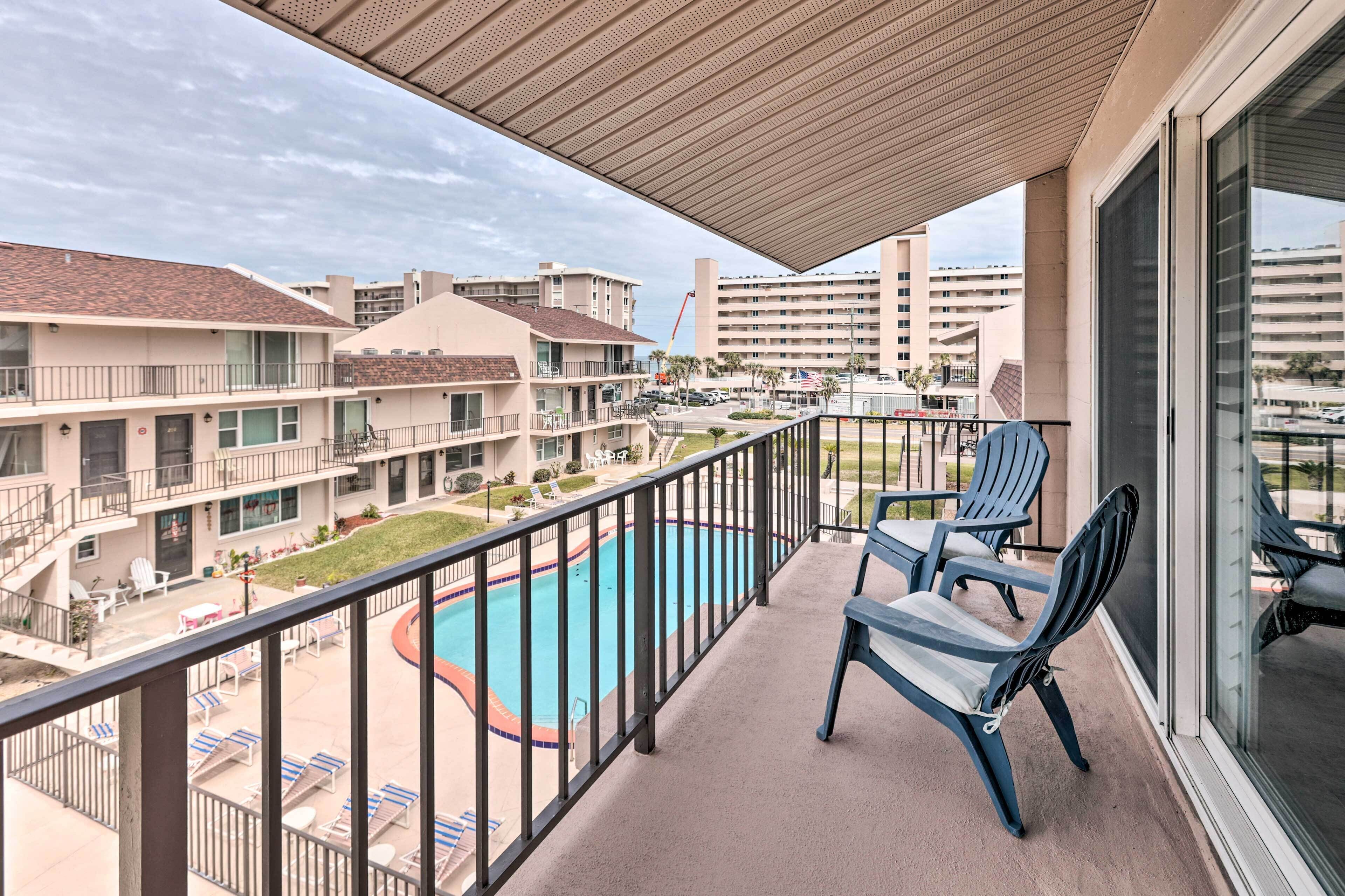 A balcony with a pool, lounge chairs, and a view of surrounding buildings.
