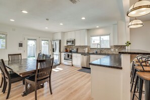 A modern kitchen with white cabinets, stainless steel appliances, and a wooden dining table with chairs.