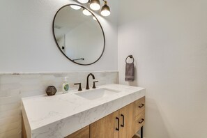 A bathroom with a white marble sink, a round mirror, and wooden cabinets.