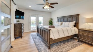 A bedroom with a wooden bed, a ceiling fan, a TV mounted on the wall, and a large window. - Private Pool & Patio: Modern Lake Havasu Home! (Lake Havasu City)