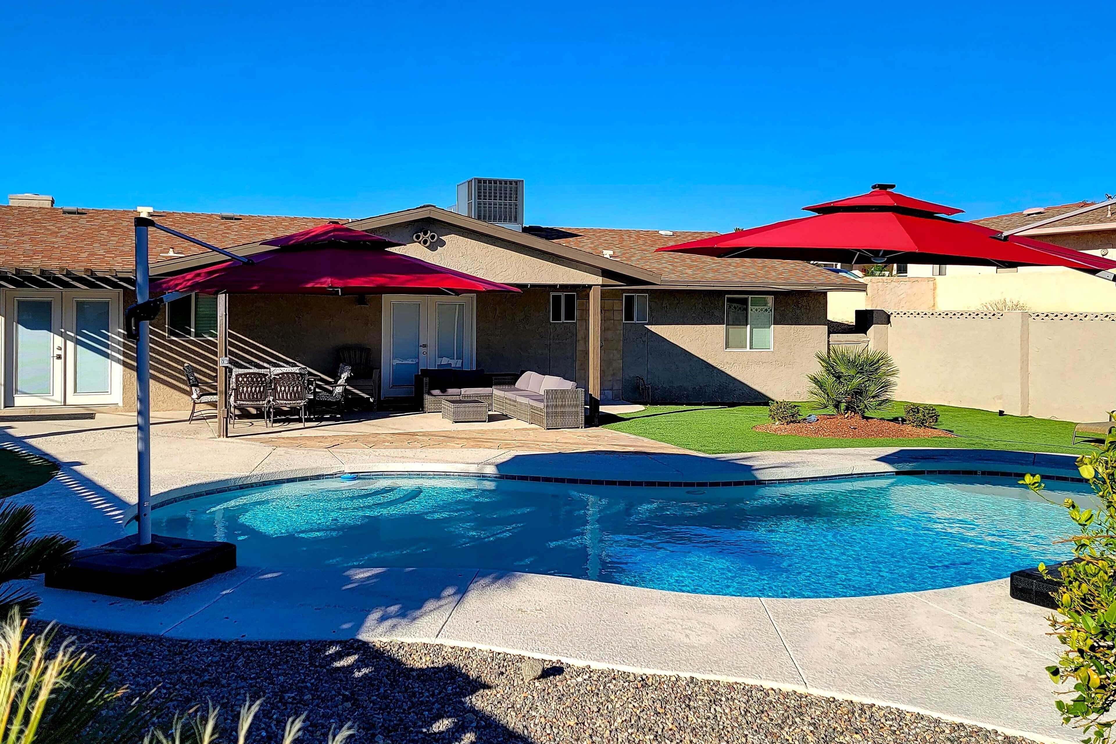 Ein Garten mit Swimmingpool, Terrassenmöbeln und roten Sonnenschirmen.