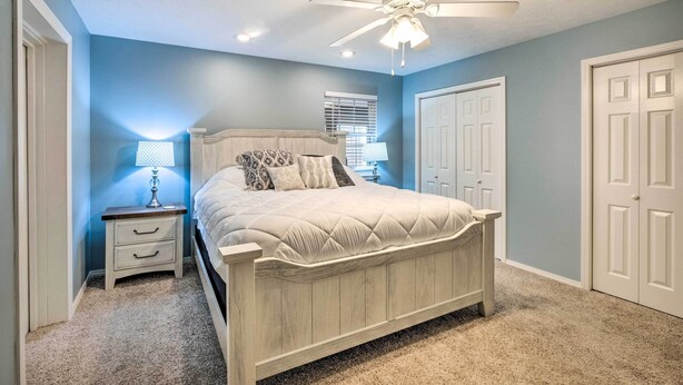 A bedroom with a bed, nightstand, lamp, ceiling fan, and two doors. - Holiday Island Home: Fire Pit & Boat Parking! (Eureka Springs)