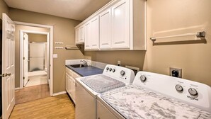 A laundry room with a washer and dryer, a countertop with a sink, and cabinets above the appliances. - Holiday Island Home: Fire Pit & Boat Parking! (Eureka Springs)