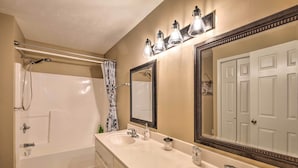 A bathroom with a bathtub, two sinks, a large mirror, and a shower curtain. - Holiday Island Home: Fire Pit & Boat Parking! (Eureka Springs)