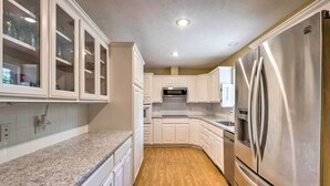 A kitchen with white cabinets, a stainless steel refrigerator, and a granite countertop. - Holiday Island Home: Fire Pit & Boat Parking! (Eureka Springs)