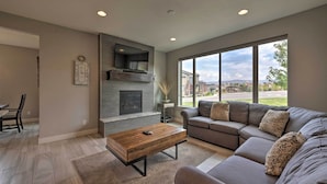 A modern living room with a fireplace, a large window, and a sectional sofa. - Modern Huntsville Resort Retreat w/ Deck & Hot Tub (Huntsville)