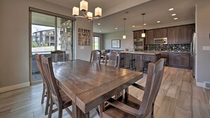 A spacious dining area with a large wooden table and chairs, a kitchen with dark wooden cabinets, and a view through a glass door to the outside. - Modern Huntsville Resort Retreat w/ Deck & Hot Tub (Huntsville)
