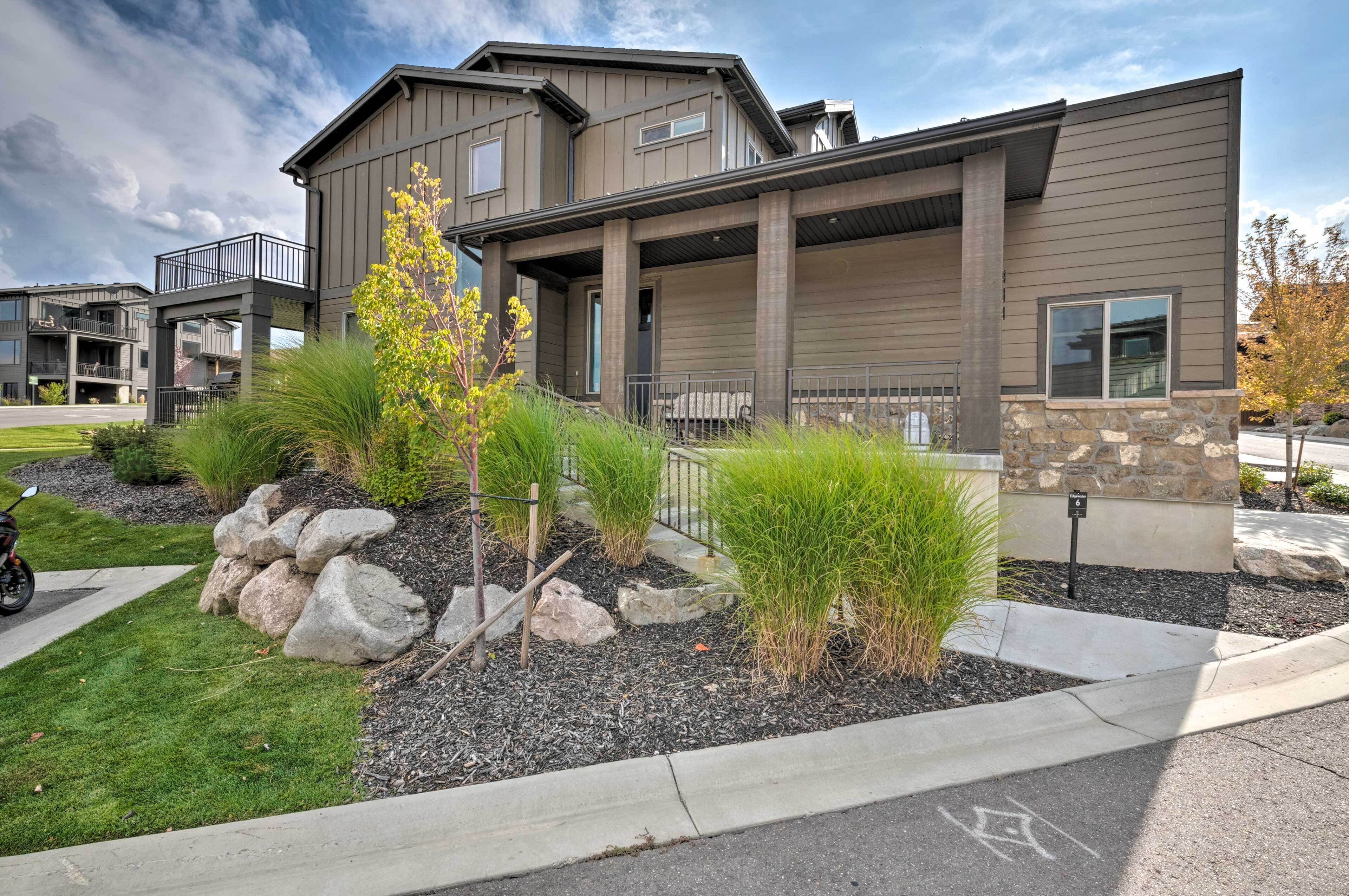 A modern two-story residential building with a stone accent wall, a covered porch, and a landscaped front yard with rocks and shrubs.