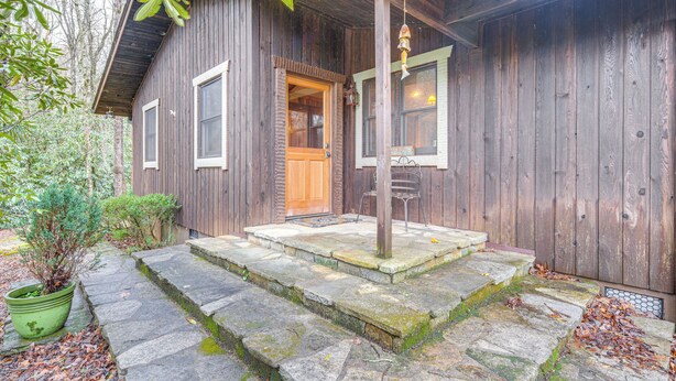 Eine rustikale Holzhütte mit einer Steintreppe, die zu einer Holztür führt, umgeben von viel Grün.