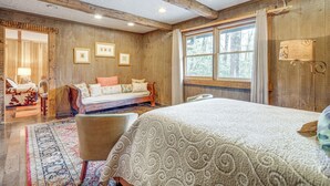 Ein gemütliches Schlafzimmer mit einem großen Bett, einem Holzkopfteil, einem Fenster mit Vorhängen, einer Nachttischlampe und einem gerahmten Bild an der Wand.