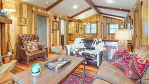 Ein gemütliches Wohnzimmer mit Holzwänden, einem Ledersessel, einem Sofa aus Rindsleder und einem Couchtisch mit Dekoration.