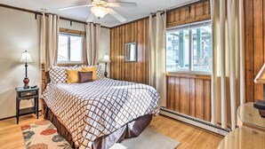 Une chambre avec un grand lit, des murs recouverts de panneaux de bois, un ventilateur de plafond et une fenêtre avec des rideaux.