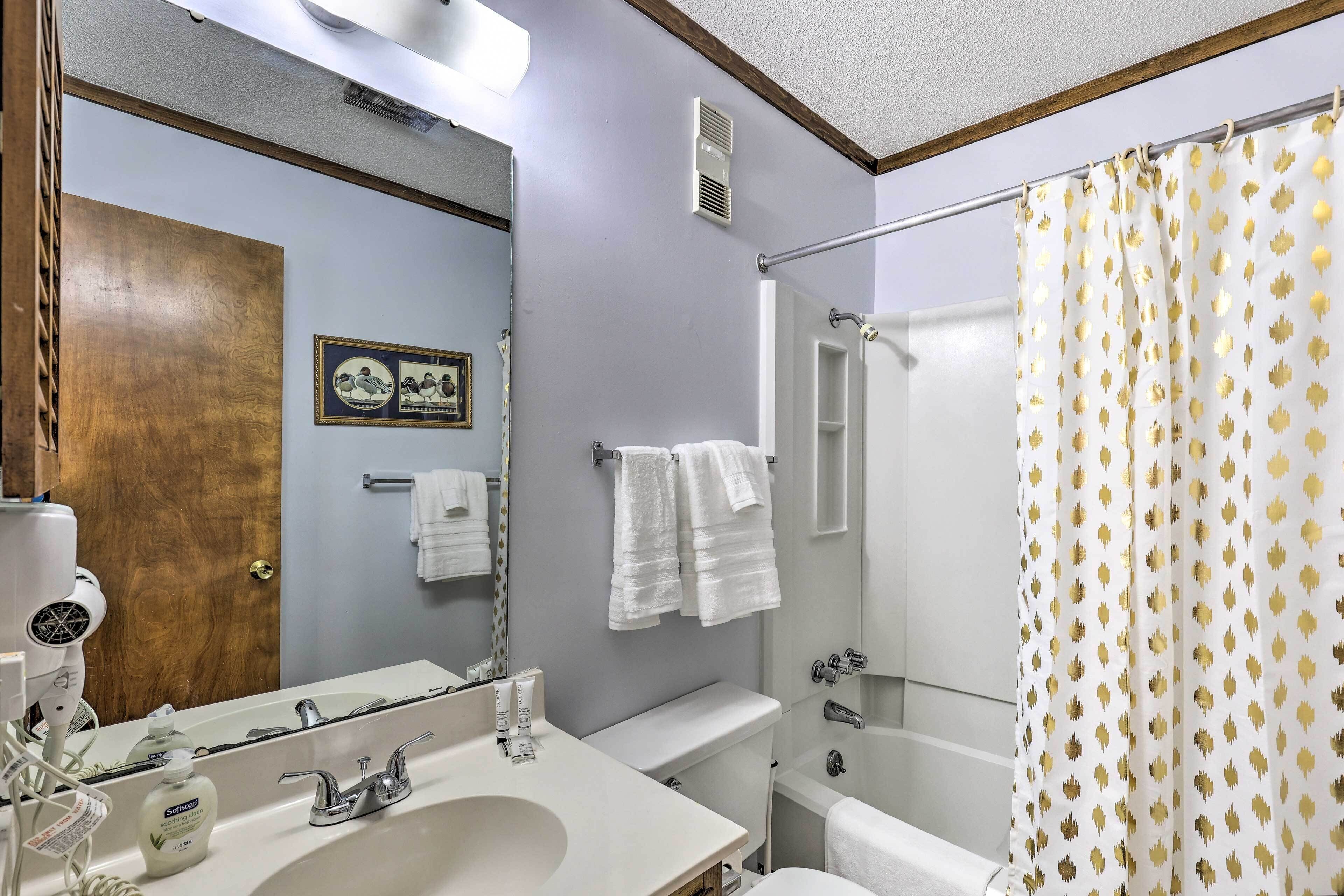 Un baño con lavamanos, espejo y cortina de ducha con diseño de hojas.