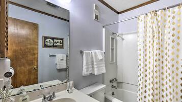 A bathroom with a sink, mirror, and a shower curtain with a leaf pattern.