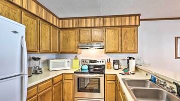 Una cocina con armarios de madera, un refrigerador de acero inoxidable, un microondas, un hervidor y un lavamanos.