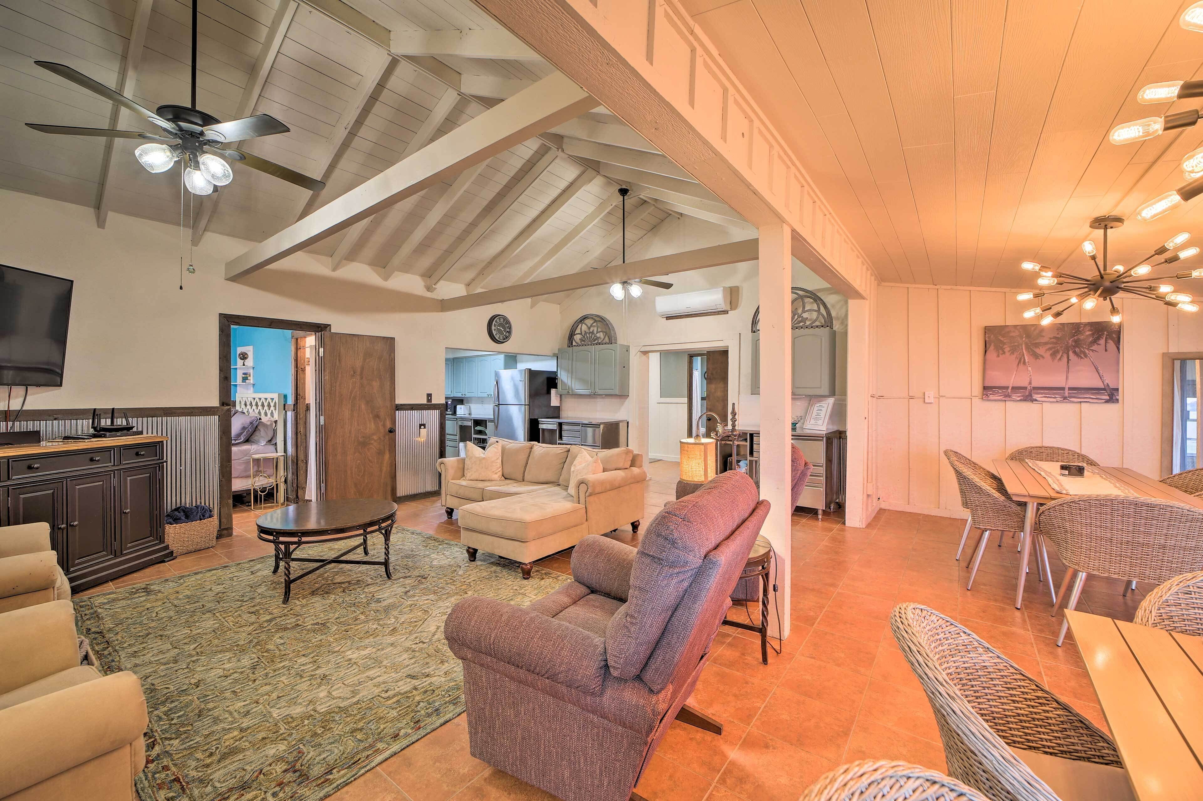 A spacious living area with a high ceiling, a ceiling fan, a dining area with wicker furniture, and a kitchen in the background.