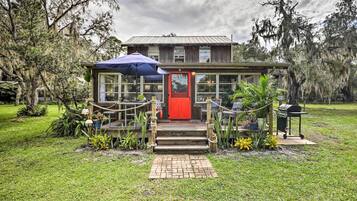 A rustic wooden building with a red door, surrounded by a well-maintained lawn and various plants.