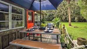 Une terrasse en bois avec une table dressée pour le repas, entourée de plantes en pot et offrant une vue sur un jardin luxuriant.