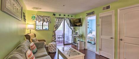 A living room with a sofa, coffee table, and a television. There is a door leading to another room.