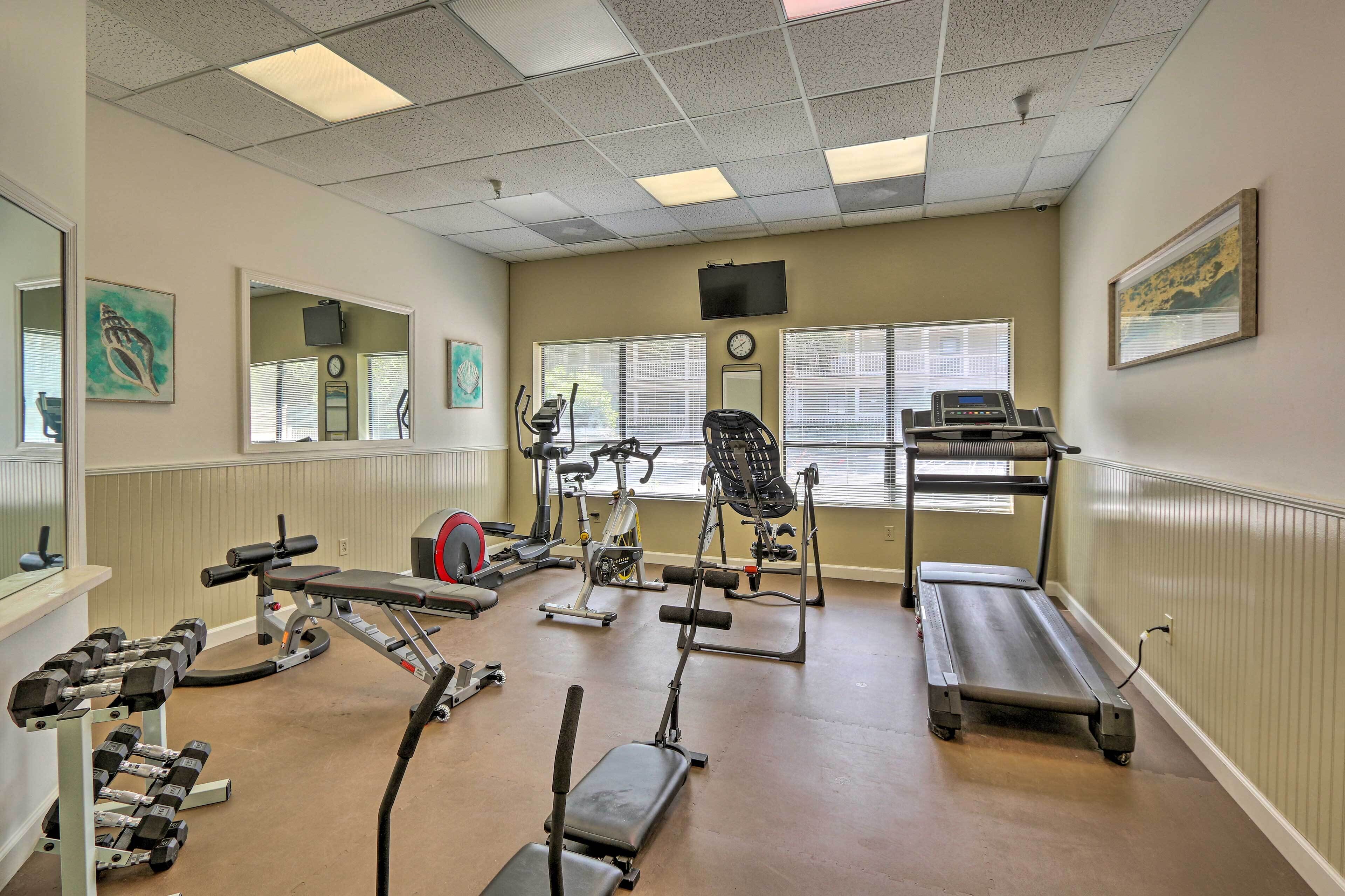 Un gimnasio con equipo de ejercicio, espejos, ventanas y una cinta de correr.