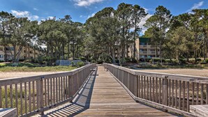 A wooden boardwalk leading to a building complex surrounded by trees. - Beach + Pool Access: Colorful Hilton Head Condo! (Hilton Head Island)