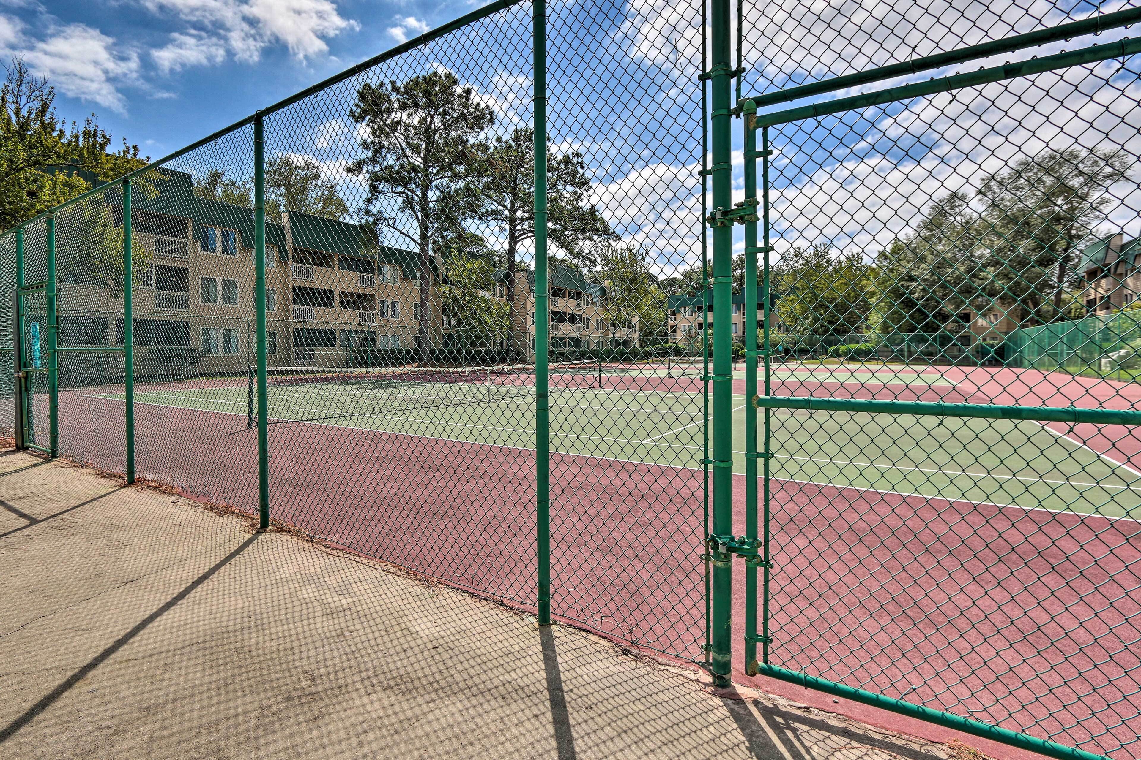 A tennis court with a green fence and a building in the background.