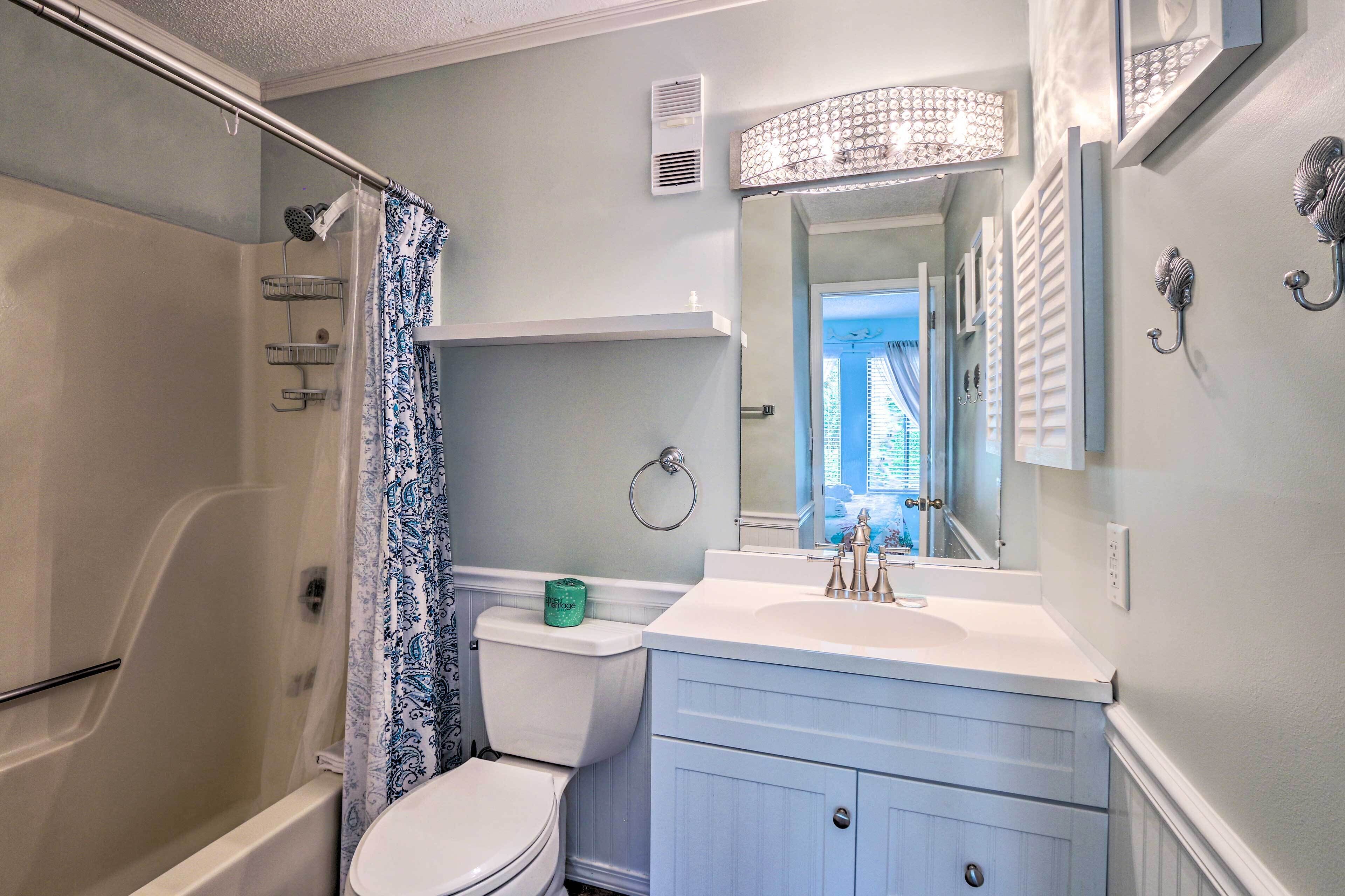 A bathroom with a shower, toilet, vanity, and a mirror.