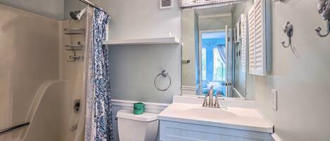 A bathroom with a shower, toilet, vanity, and a mirror.