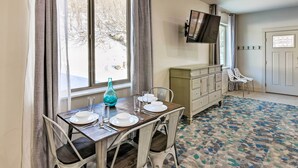 A dining area with a table set for four, a TV mounted above the table, and a view of the outdoors through large windows. - Anchorage Studio Escape ~ 14 Miles From Downtown! (Anchorage)