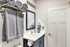 A bathroom with a white sink, dark blue cabinets, a mirror, and a towel rack with rolled towels. - Anchorage Studio Escape ~ 14 Miles From Downtown! (Anchorage)