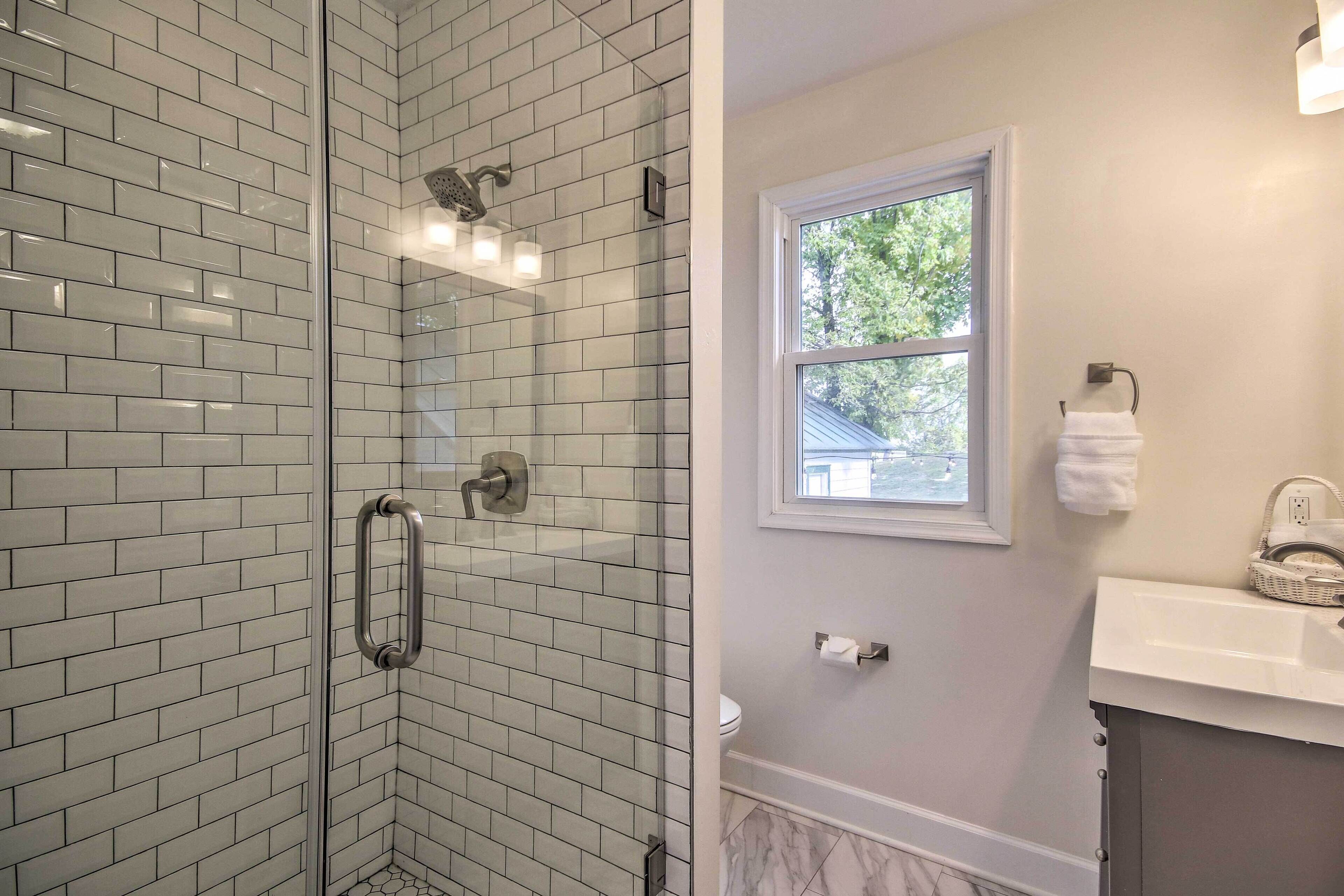 Un baño con cabina de ducha de vidrio, un lavabo blanco y un ventanal que proporciona luz natural.