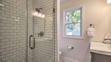 Un baño con cabina de ducha de vidrio, un lavabo blanco y un ventanal que proporciona luz natural.