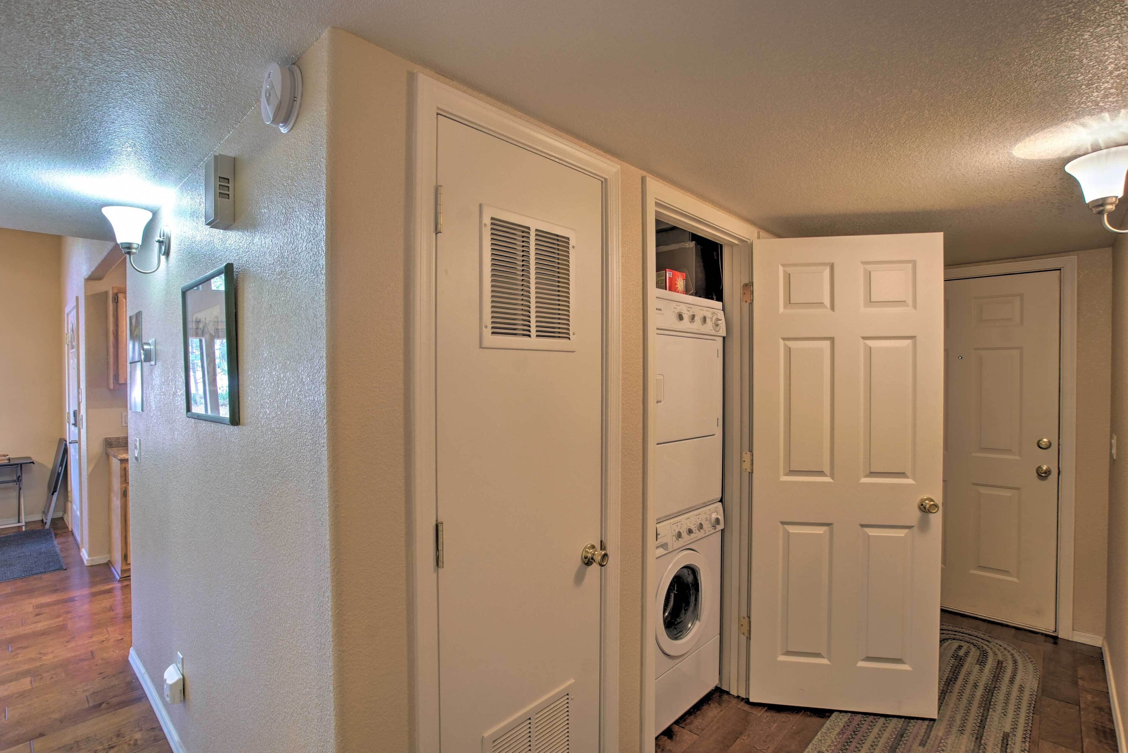 A laundry room with a washer and dryer, a door with a vent, and a hallway with wooden flooring and a rug.