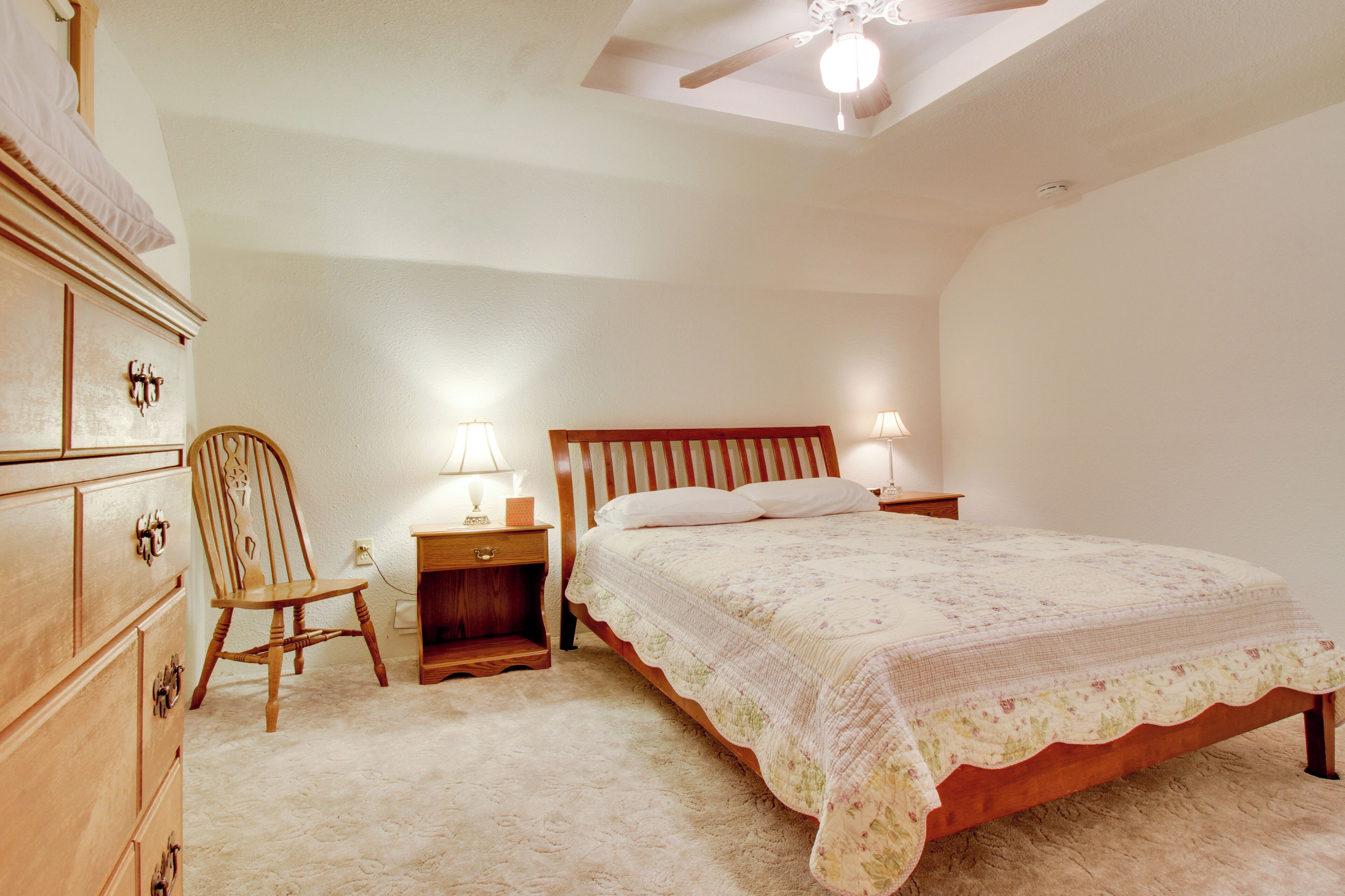 Un dormitorio con cama de madera, cómoda de madera, una silla y mesita de noche con lámparas.