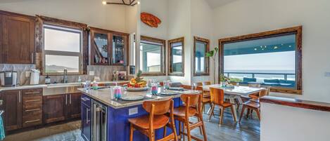 A spacious kitchen with a large island, wooden cabinets, and a view of the ocean through the windows.
