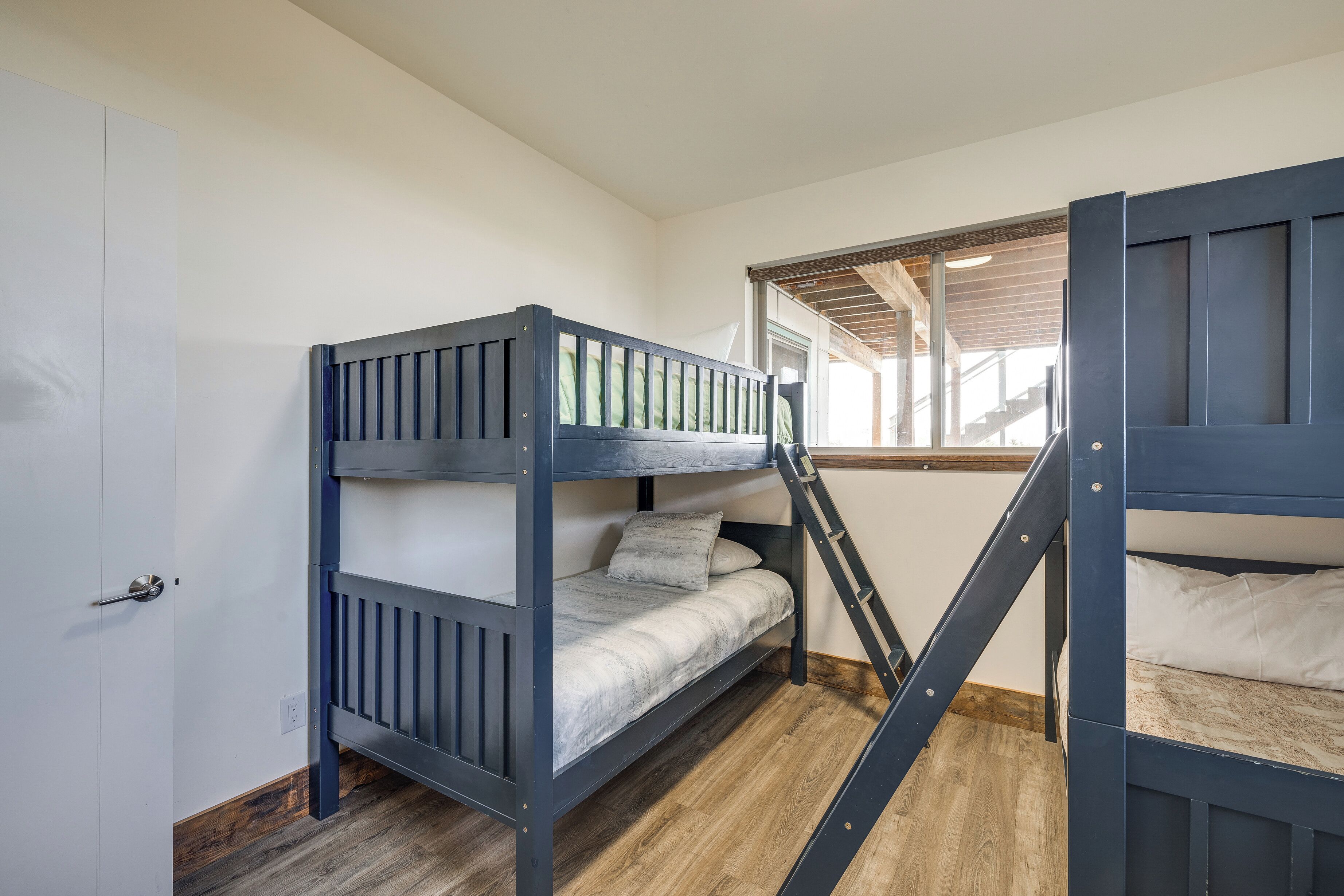 Une chambre avec des lits superposés, un plancher en bois, des murs blancs et une fenêtre donnant sur l’extérieur.