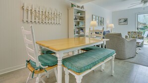 Un coin repas avec une table en bois et des chaises blanches, une bibliothèque et une vue sur l’extérieur.