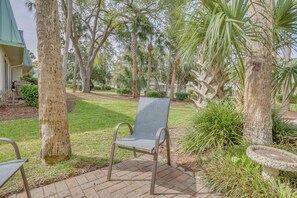 Un espace patio aménagé avec une chaise en métal, un abreuvoir pour oiseaux et un palmier.