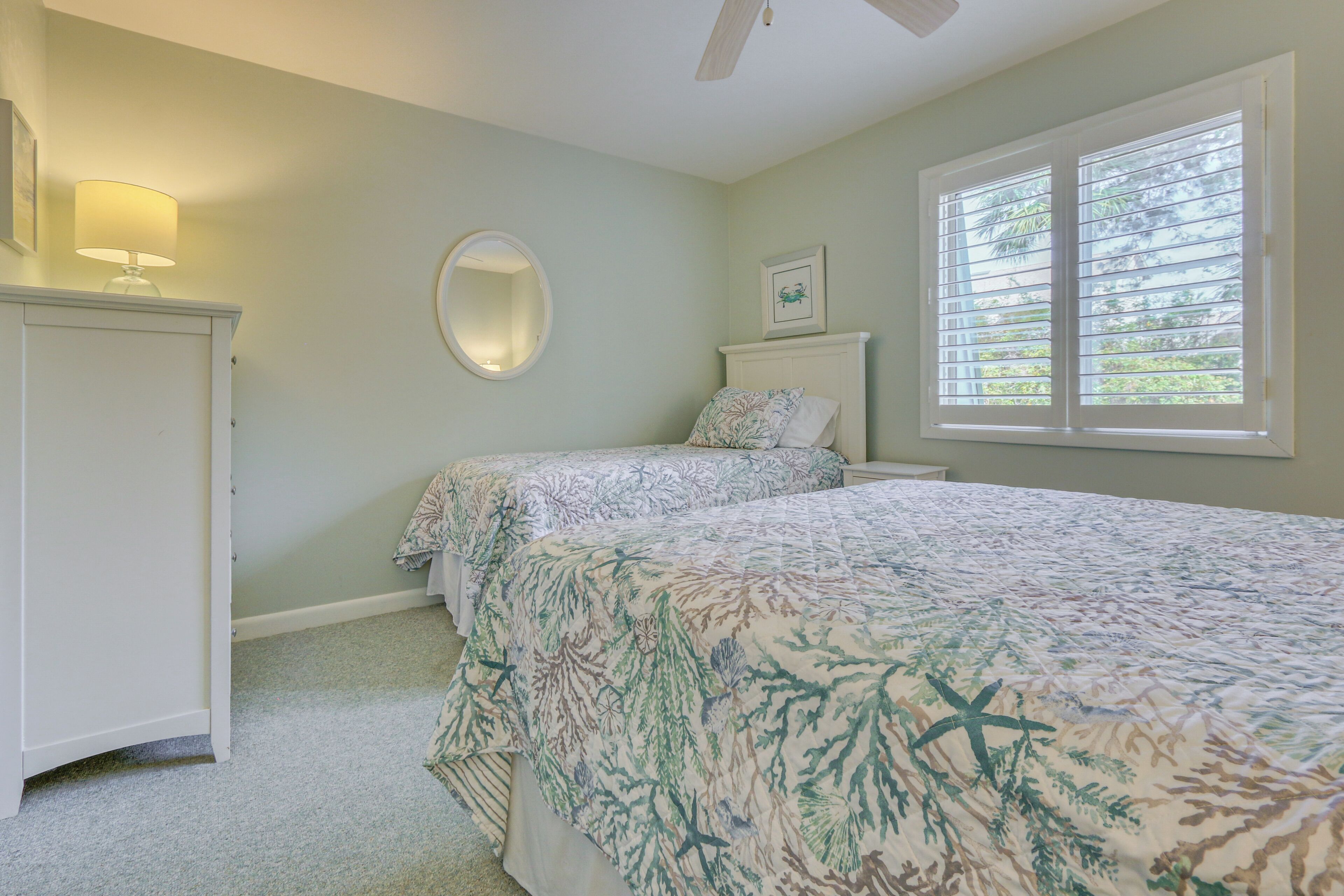 A bedroom with two beds, a dresser, a mirror, and a window with blinds.