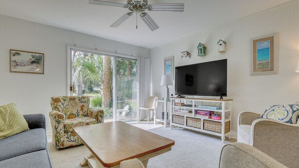 Un salon avec un téléviseur, un ventilateur de plafond, une table basse et une bibliothèque.