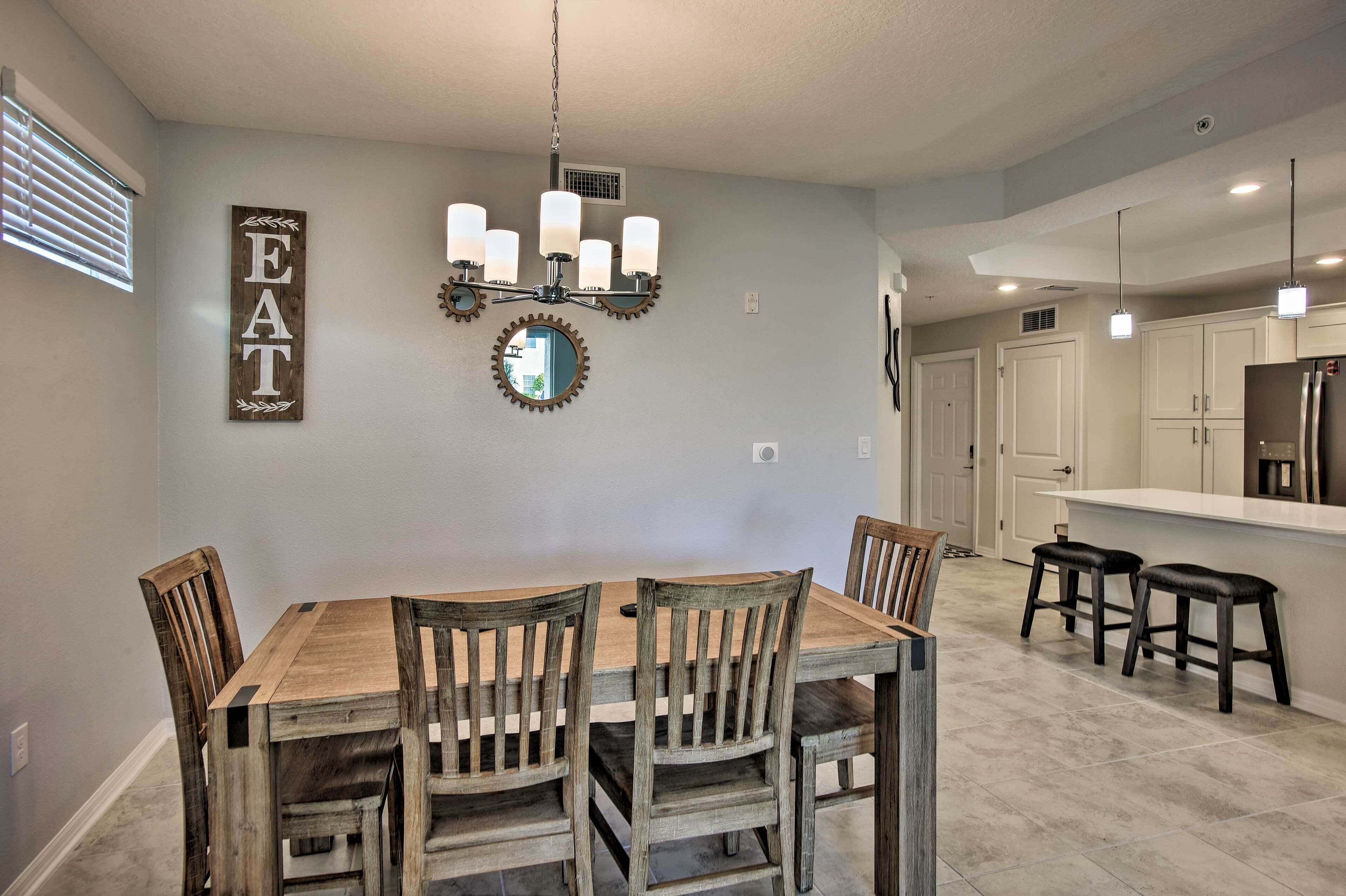 A dining area with a wooden table and chairs, a chandelier, and a wall-mounted mirror.