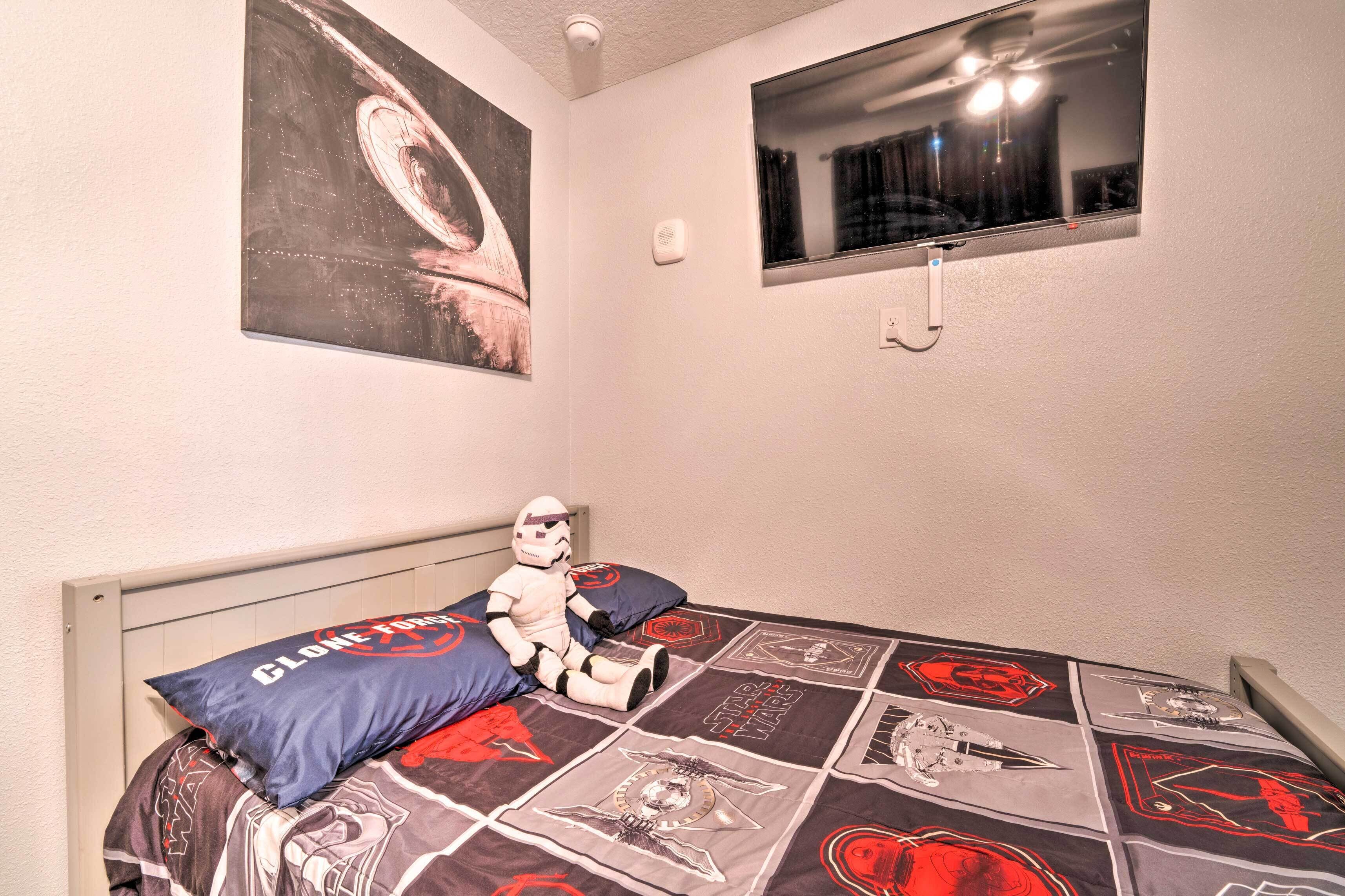 Een slaapkamer met een Star Wars sprei, een groot schilderij aan de muur en een raam met uitzicht op de nachthemel.