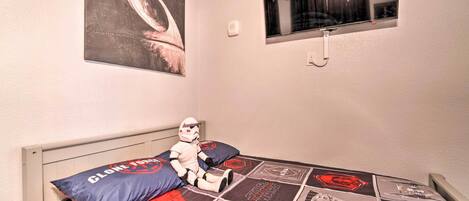 A bedroom with a Star Wars themed bedspread, a large painting on the wall, and a window with a view of the night sky.