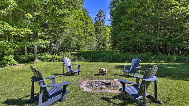 A fire pit surrounded by Adirondack chairs in a grassy area with trees in the background. - Cozy Florence Cabin, Proximity to Keyes Peak! (Florence)