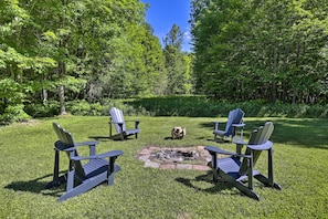 A fire pit surrounded by Adirondack chairs in a grassy area with trees in the background. - Cozy Florence Cabin, Proximity to Keyes Peak! (Florence)